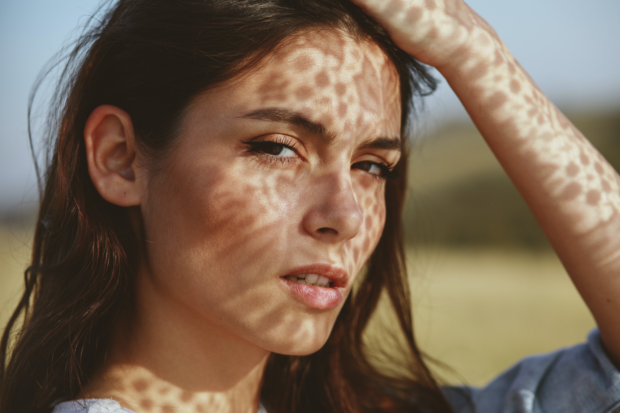 Portrait of a young woman with shadows texture on the face in a meadow with